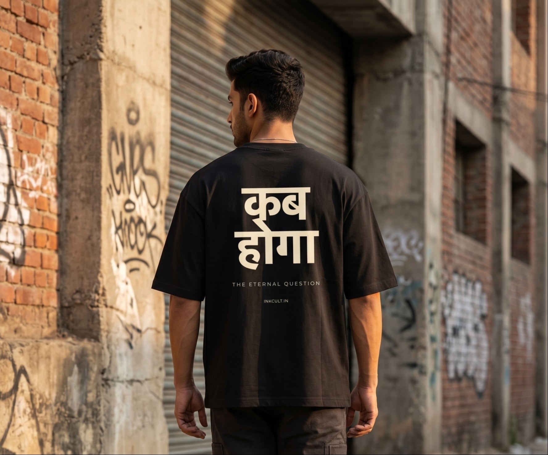 Person wearing a black t-shirt with white text standing in front of a brick wall with graffiti.